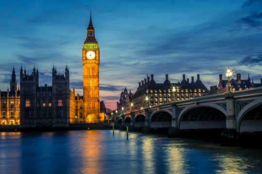 Big Ben and Houses of Parliament illuminated at twilight, reflected in the Thames River with Westminster Bridge