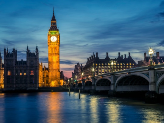 Big Ben and Houses of Parliament illuminated at twilight, reflected in the Thames River with Westminster Bridge