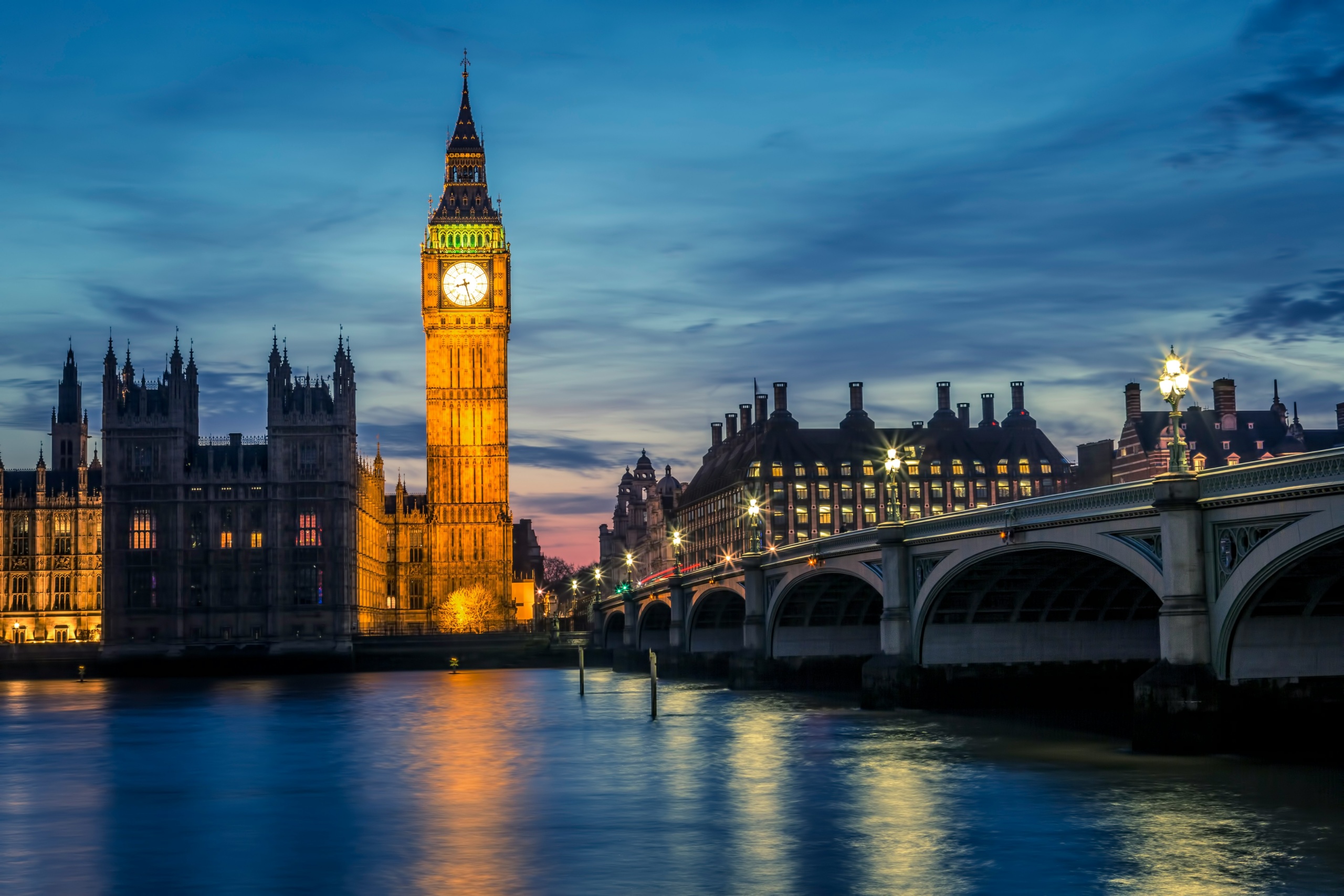 Big Ben and Houses of Parliament illuminated at twilight, reflected in the Thames River with Westminster Bridge
