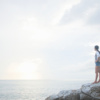 A young Asian woman hiker on vacation stands on a coastal rock with her backpack at sunrise and looks out to sea. Travel, wonderlust and achievement concepts.